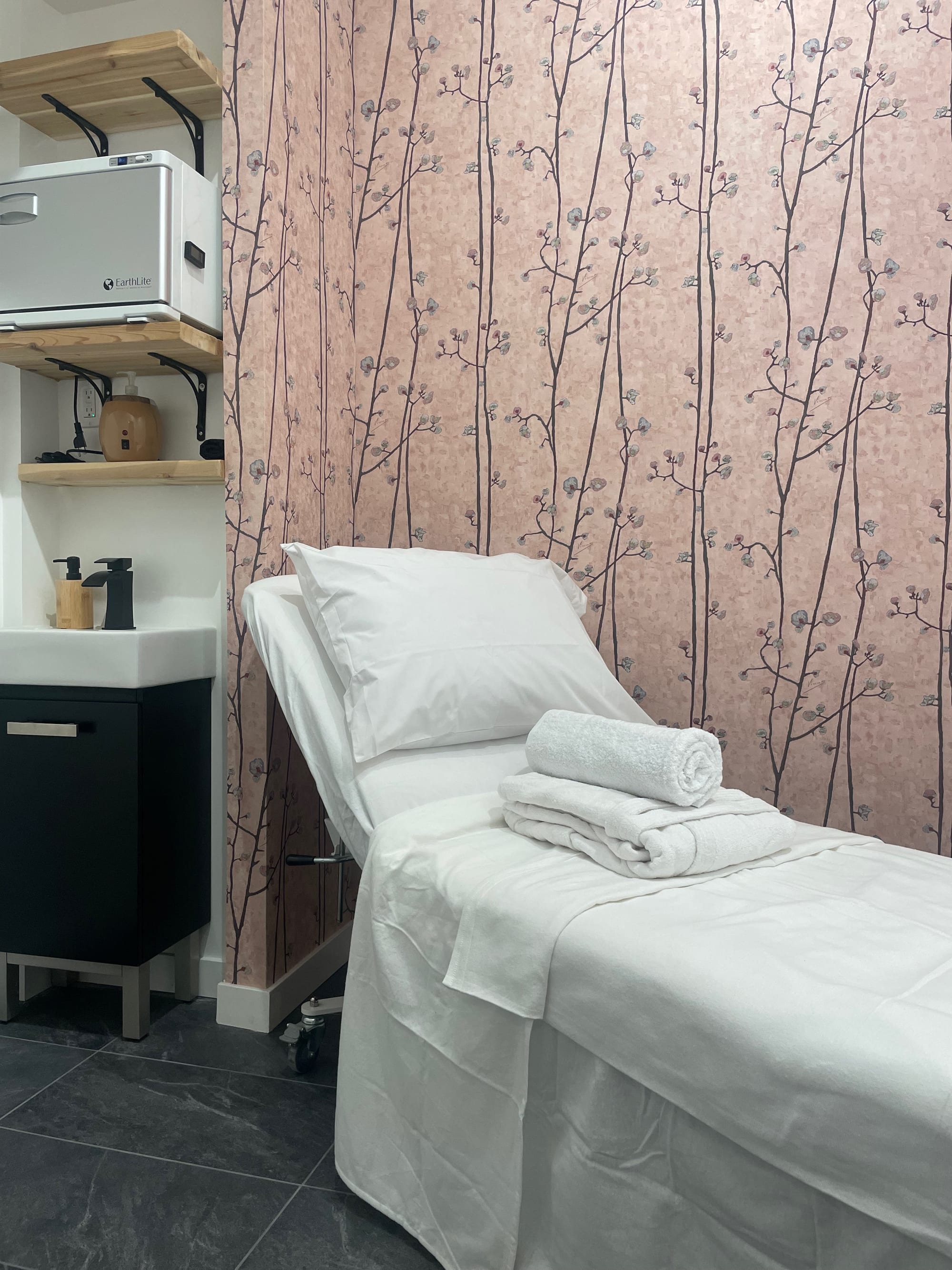 Treatment room with floral feature wall, adjustable treatment table, open shelving and integrated sink