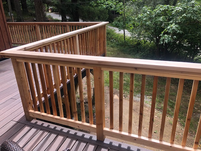 Custom composite deck — cedar vertical baluster railing against forested backdrop